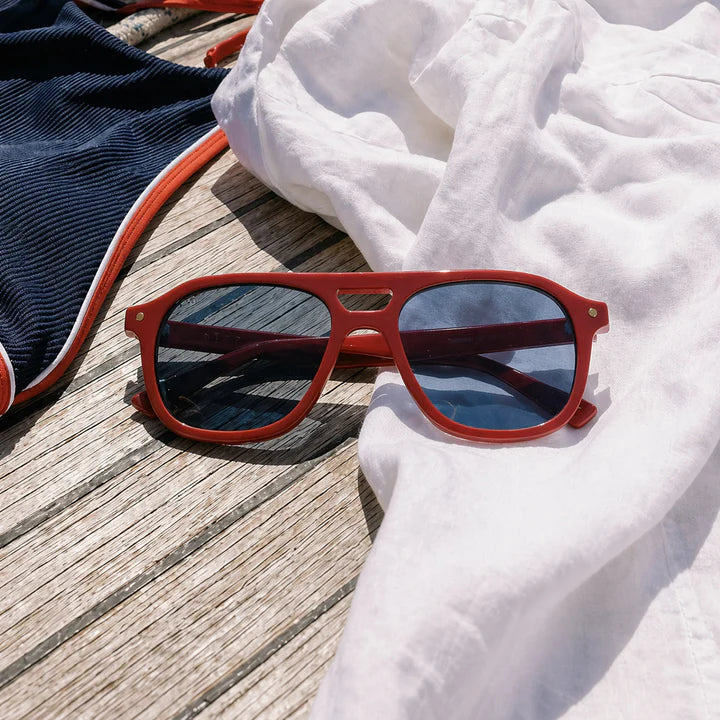 Red sunglasses on a wooden surface with a white towel and blue fabric in the background