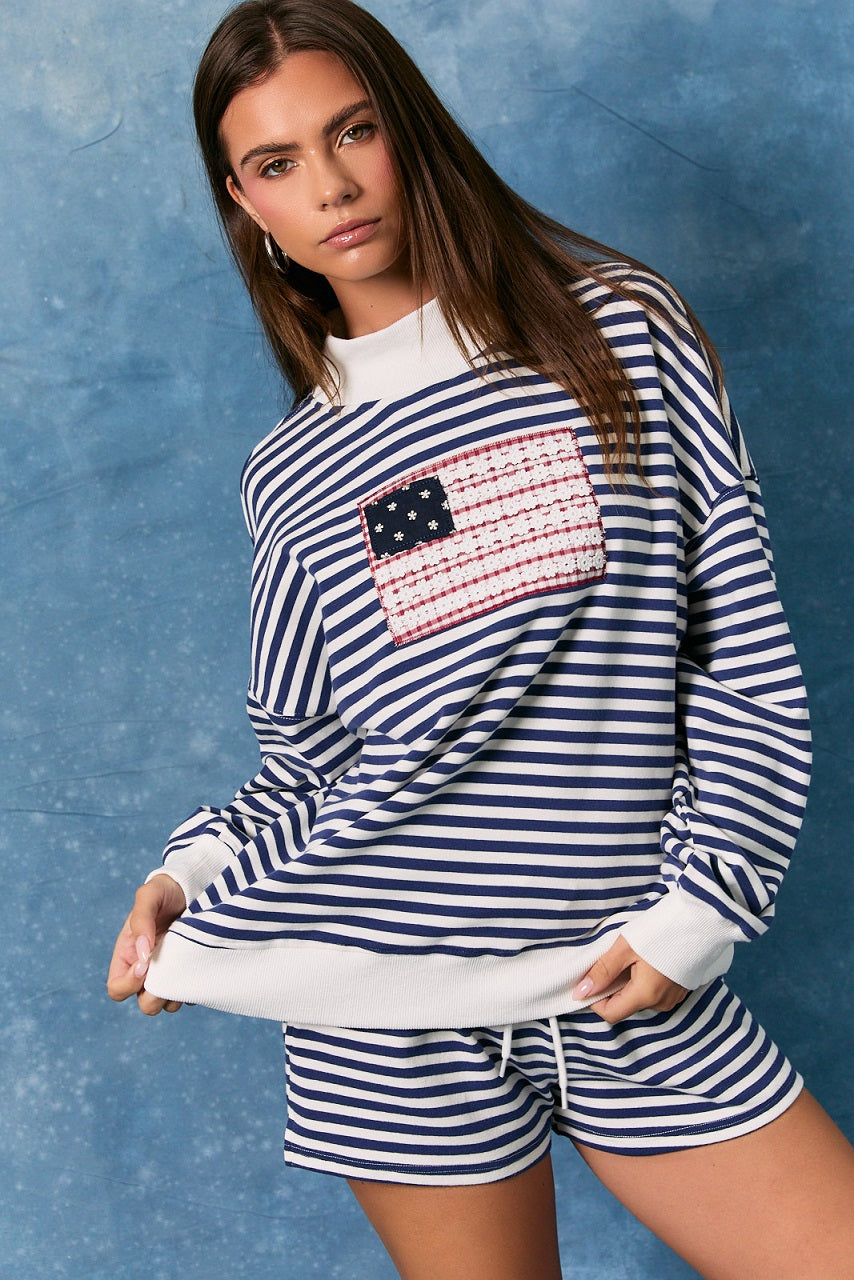 Woman wearing matching navy and white stripe sweatshirt and shorts with American flag on top on plain background