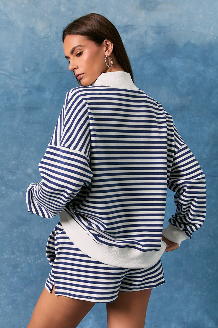 Back of woman wearing matching navy and white stripe sweatshirt and shorts on plain background