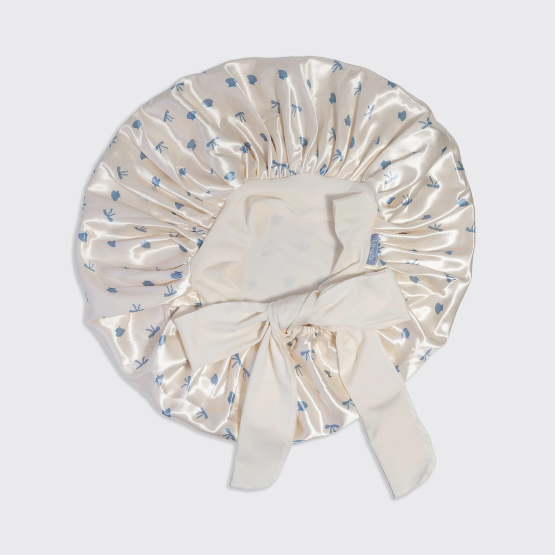 Cream-colored satin bonnet with blue floral pattern on a light gray background