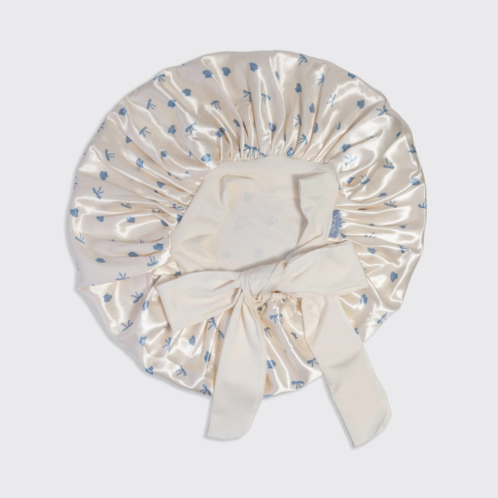 Cream-colored satin bonnet with blue floral pattern on a light gray background