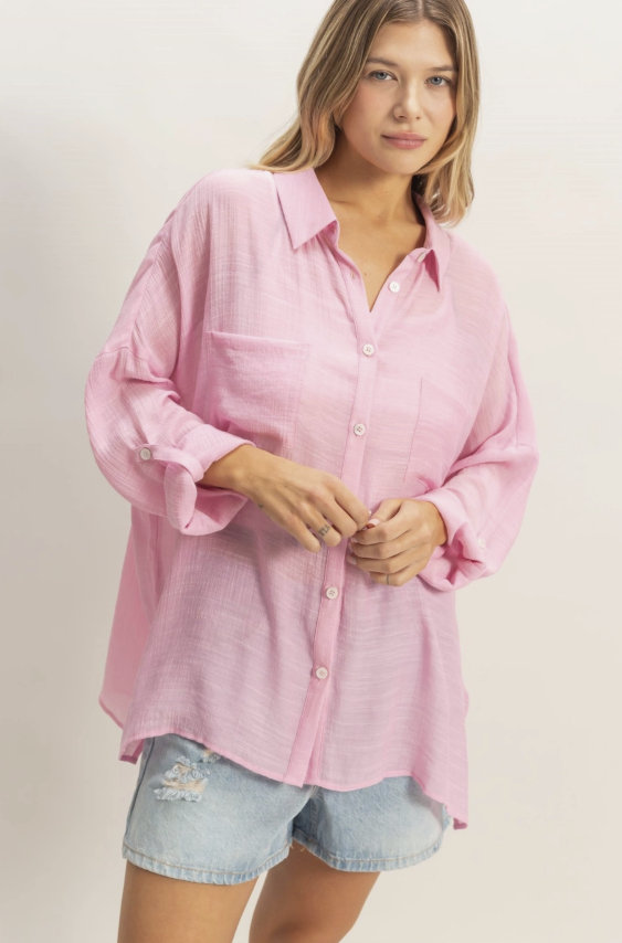 Woman wearing a pink button-up shirt and denim shorts on a plain background