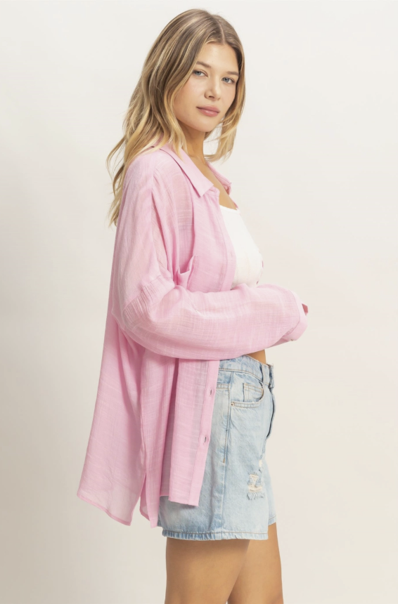 Woman wearing a pink oversized shirt and denim shorts on a plain background