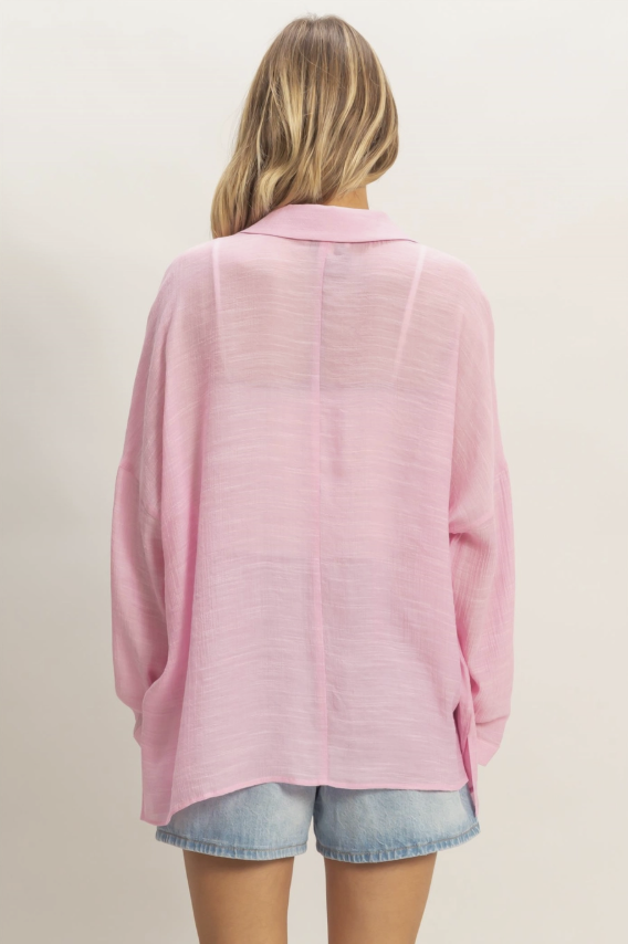 Person wearing a pink cardigan over a denim shirt on a beige background
