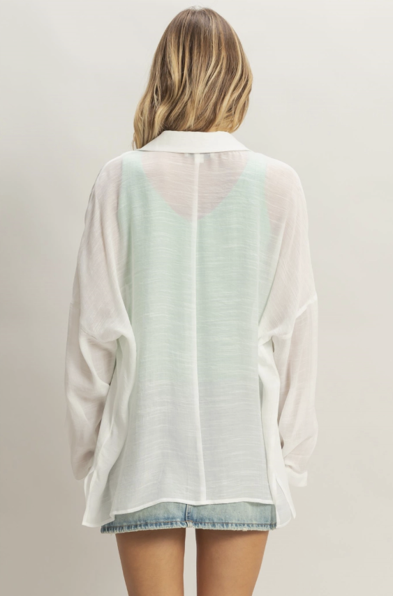 Woman wearing a sheer white blouse over a denim skirt on a plain background