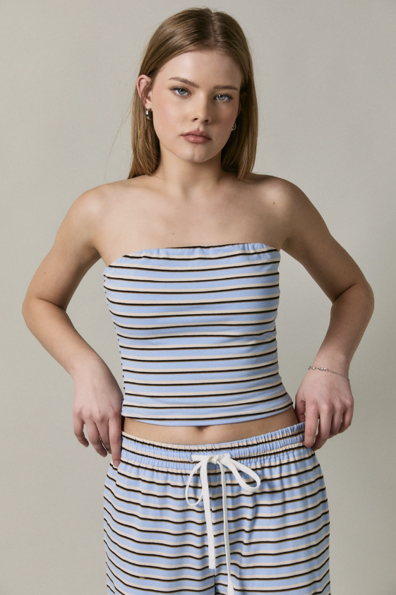 A woman modeling a matching two-piece loungewear set featuring a strapless top and drawstring shorts, both in a light blue and navy blue horizontal stripe pattern, against a solid light gray background.