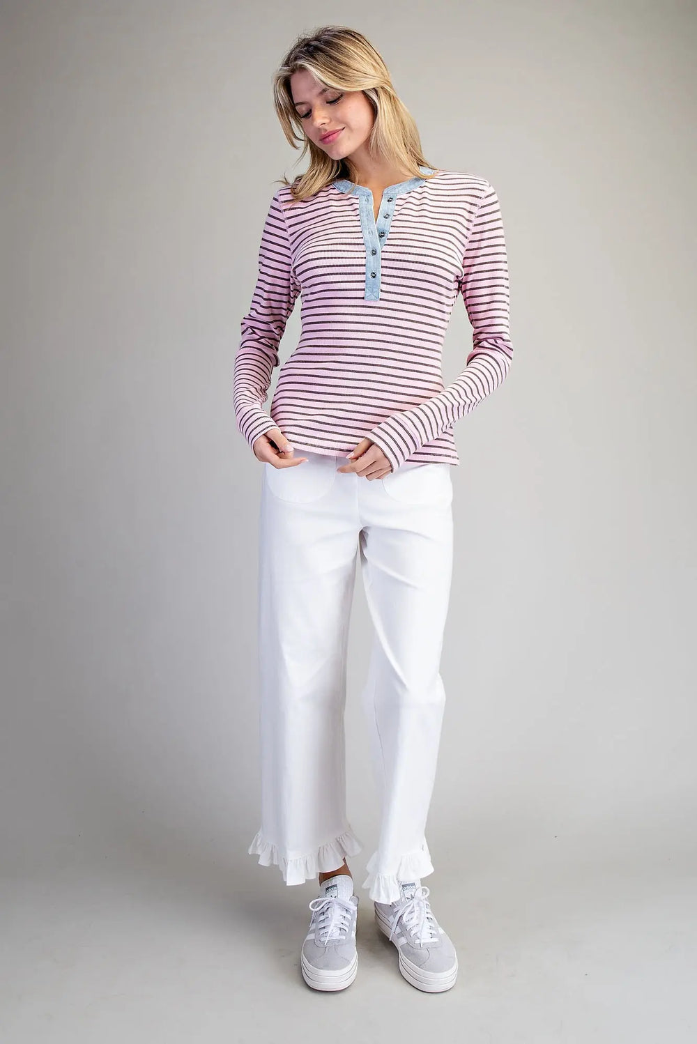 Woman wearing a striped shirt and white pants on a plain background