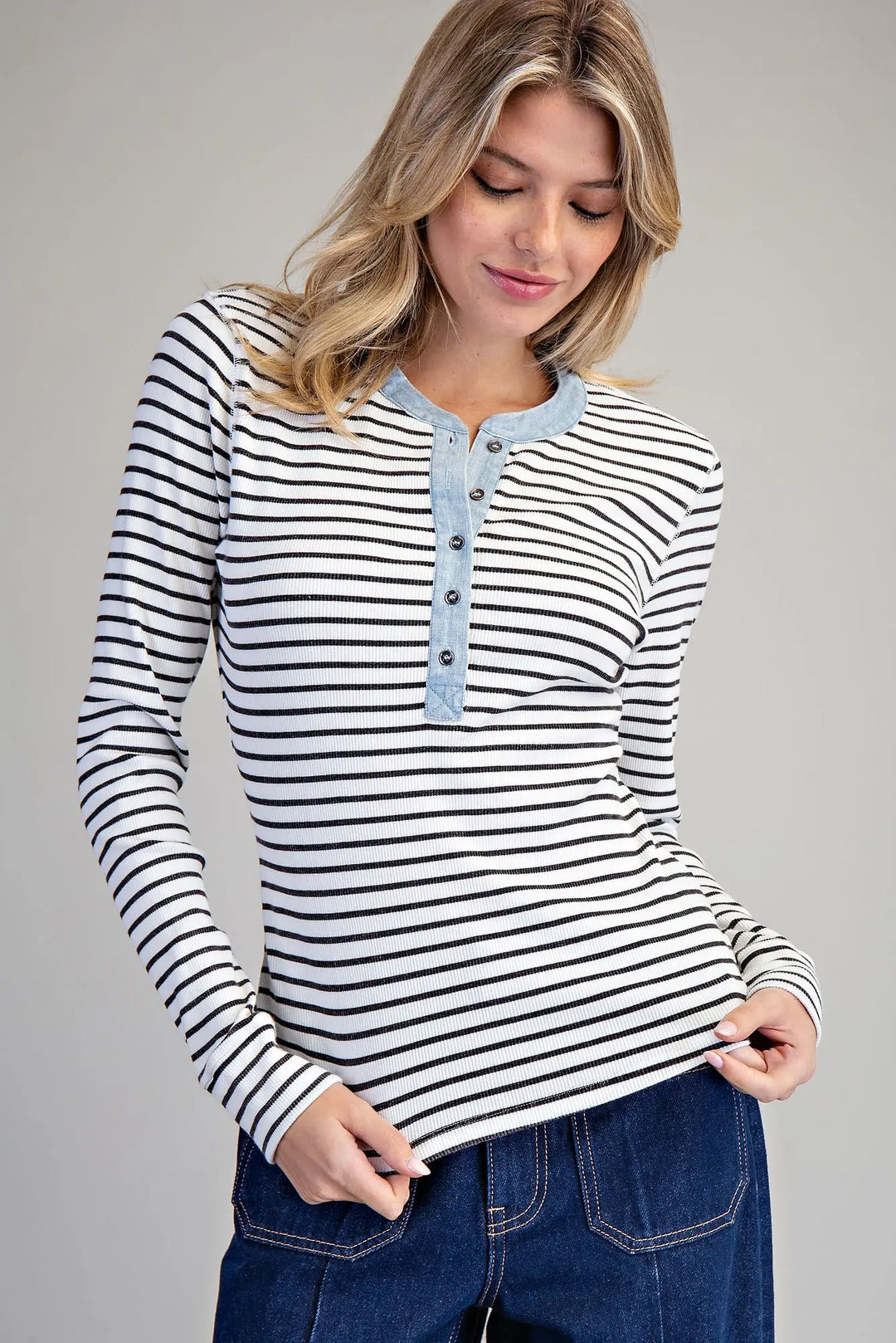 Woman wearing a black and white striped long-sleeve shirt with blue buttons on a gray background