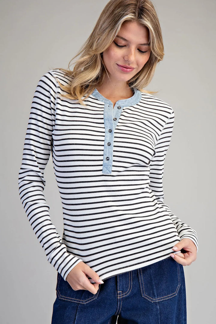 Woman wearing a black and white striped long-sleeve shirt with blue buttons on a gray background