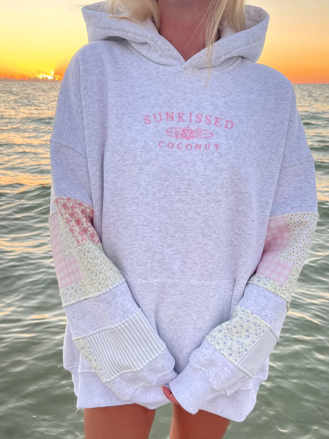 Person wearing grey sweatshirt with 'sunkissed coconut' embroidery and patchwork on the water