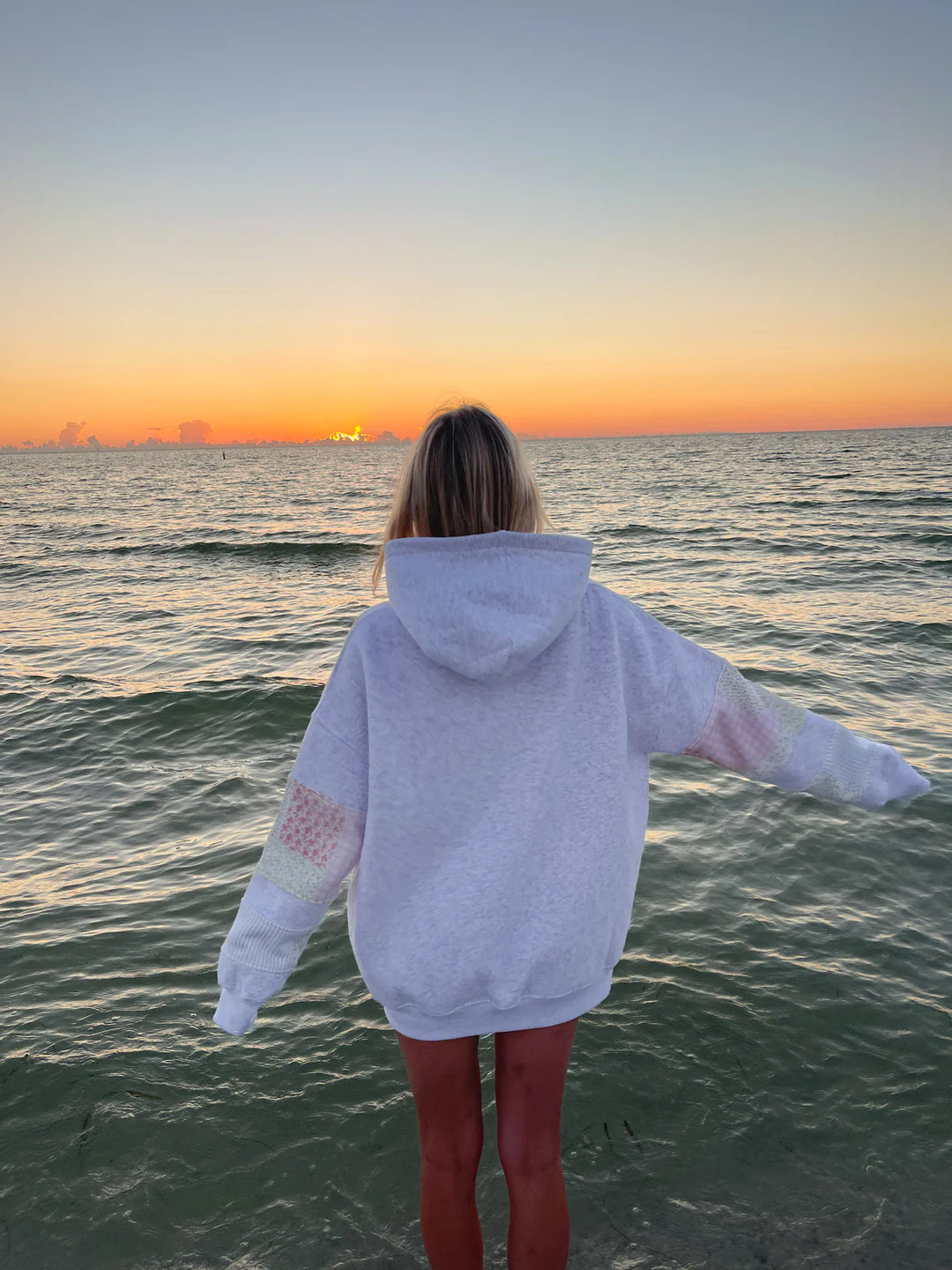 Back of woman wearing grey sweatshirt with patchwork on elbows standing in water