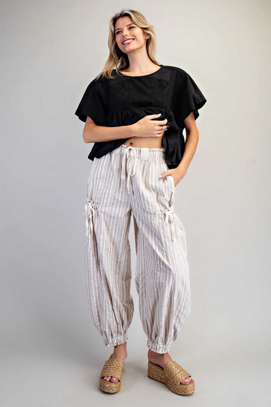 Woman wearing a black top and white striped pants on a plain background