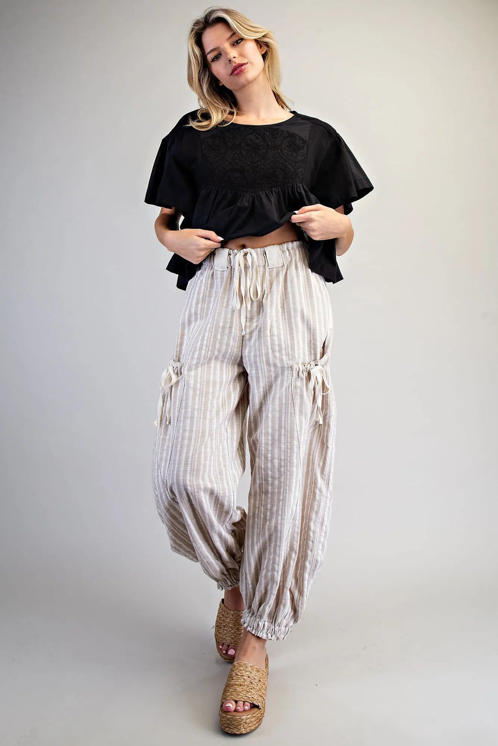 Woman wearing a black top and white striped pants on a plain background