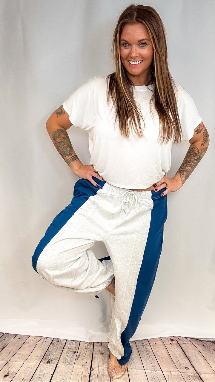 Woman wearing grey and navy stripe pants with white short sleeve top on plain background