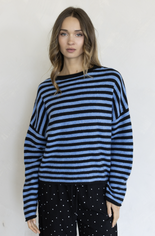 Woman wearing two tone blue stripe sweater and black pants on plain background