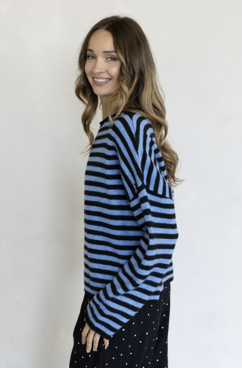 Woman wearing two tone blue stripe sweater and black pants on plain background