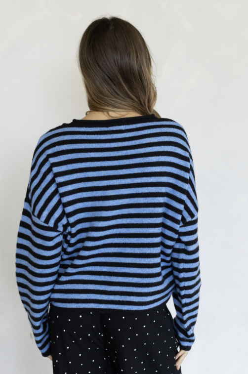 Woman shown from behind wearing two tone blue sweater and black pants on plain background