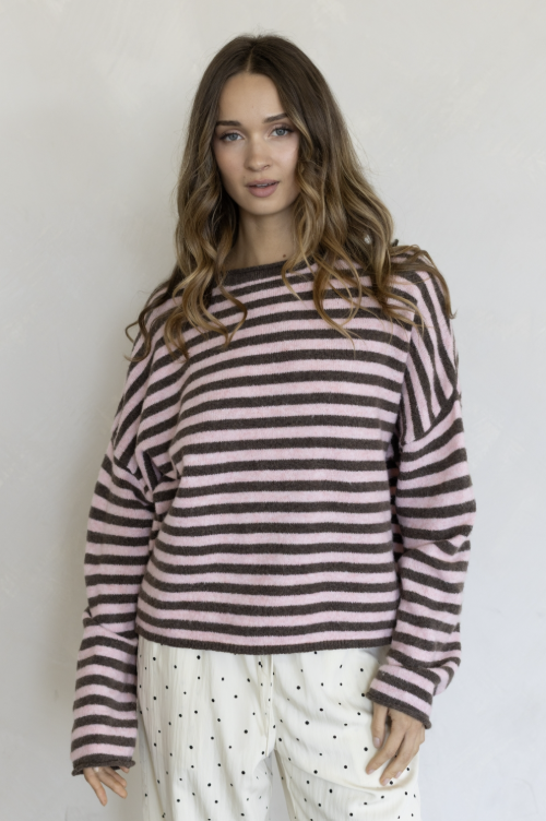 Woman wearing pink and brown stripe pullover and white pants on plain background