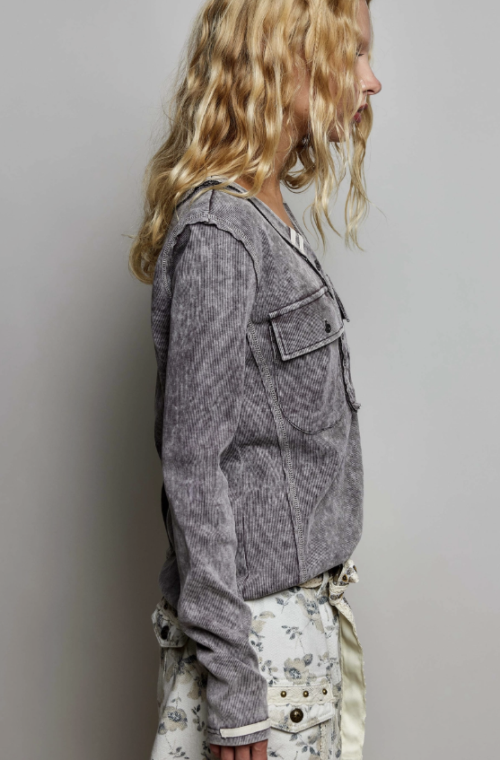 A side-profile view of a model wearing a gray textured corduroy jacket over a white floral print top and skirt, set against a plain light gray studio background.