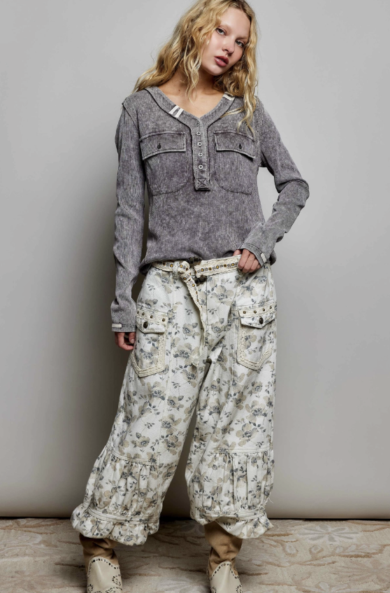 A model wearing a gray long-sleeve button-up shirt and cream-colored wide-leg floral cargo pants, standing against a neutral gray studio backdrop.
