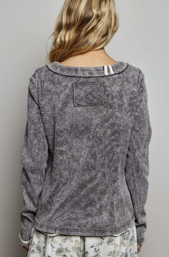 A woman viewed from the back wearing a long-sleeve gray marled or washed top with a wide boat neckline and a stitched rectangular patch detail on the upper back. The image is cropped from the shoulders to the upper thighs against a plain light gray studio background.