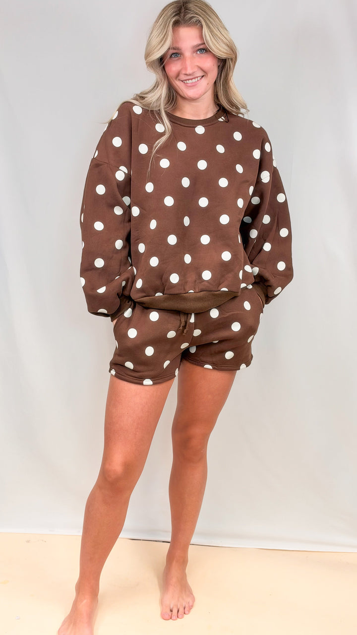 Woman wearing brown matching set with cream polka dots on plain background
