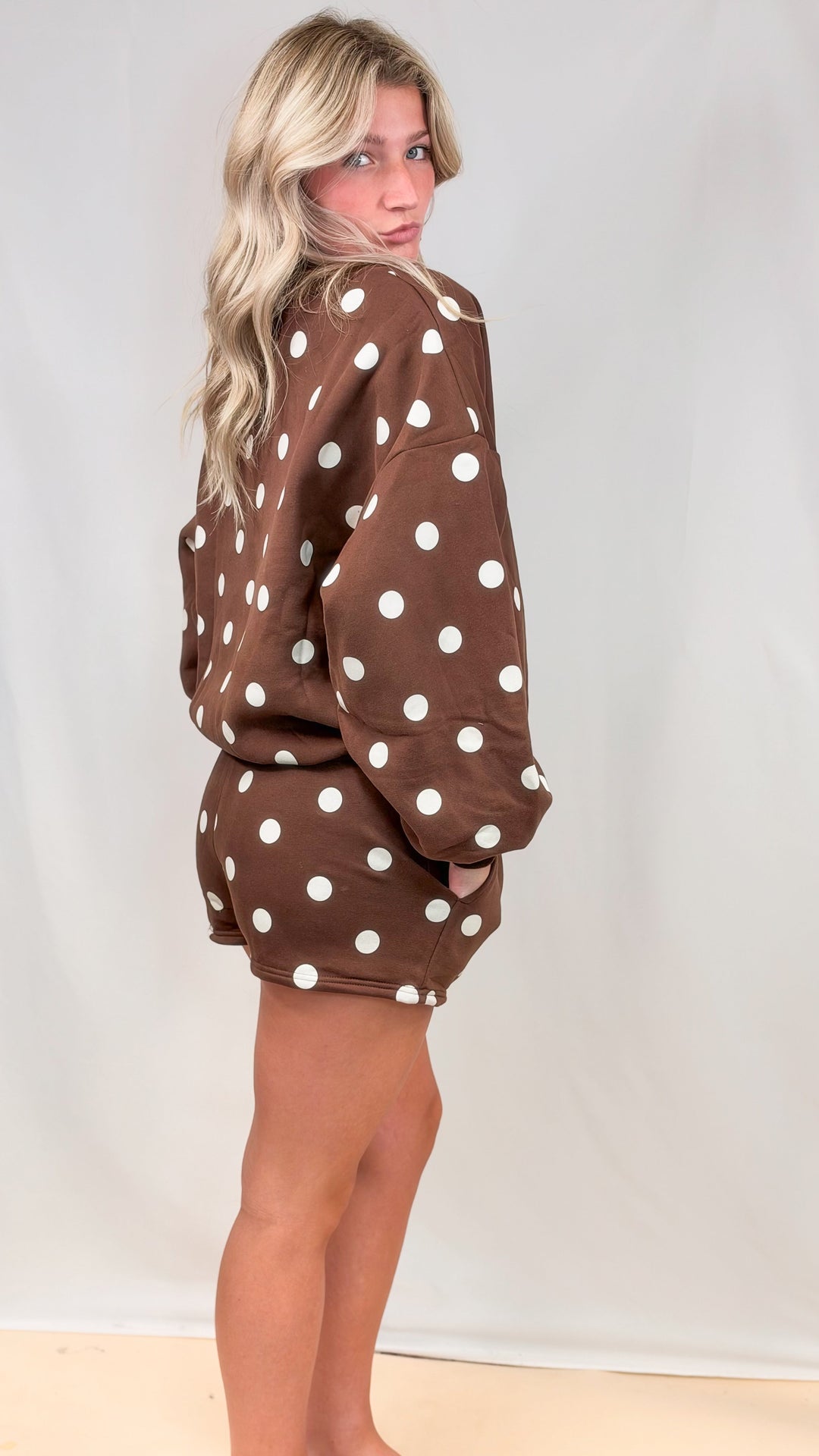 Woman shown from side view wearing brown matching set with cream polka dots on plain background