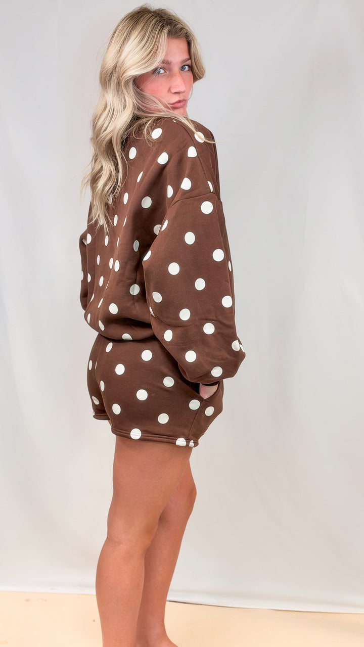 Woman shown from side view wearing brown matching set with cream polka dots on plain background