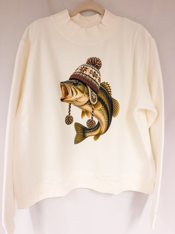 An off-white crewneck sweatshirt hanging on a wooden hanger, featuring a graphic print of a largemouth bass wearing a knit winter hat with a pom-pom.