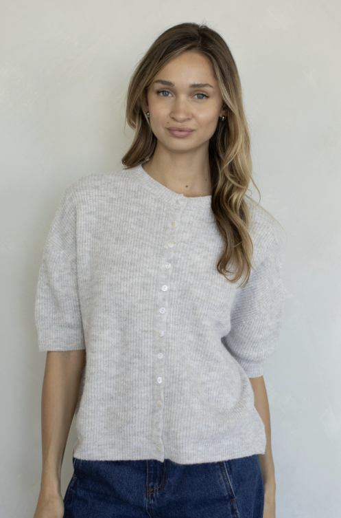 Woman wearing oatmeal colored cardigan and jeans on plain background