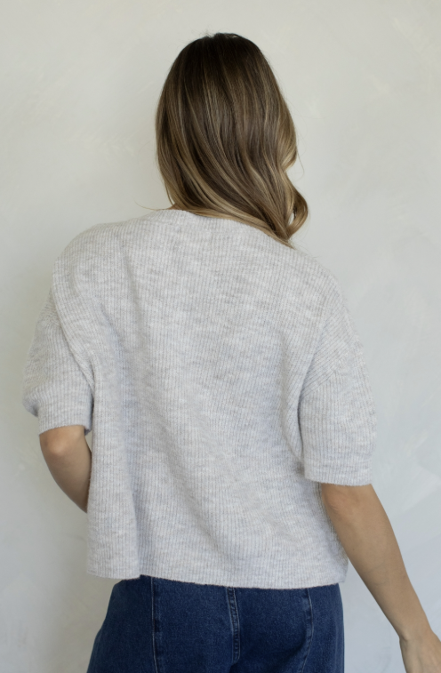 Woman shown from back wearing oatmeal cardigan and jeans on plain background