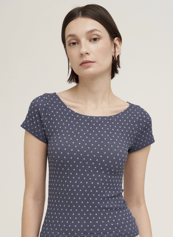 A woman wearing a navy blue short-sleeve top with a small white geometric pattern, photographed against a plain light beige studio background.