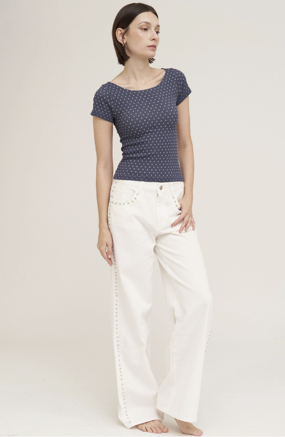 A woman modeling a navy blue short-sleeve top with a small white geometric pattern, paired with white wide-leg pants, against a plain light beige studio background.