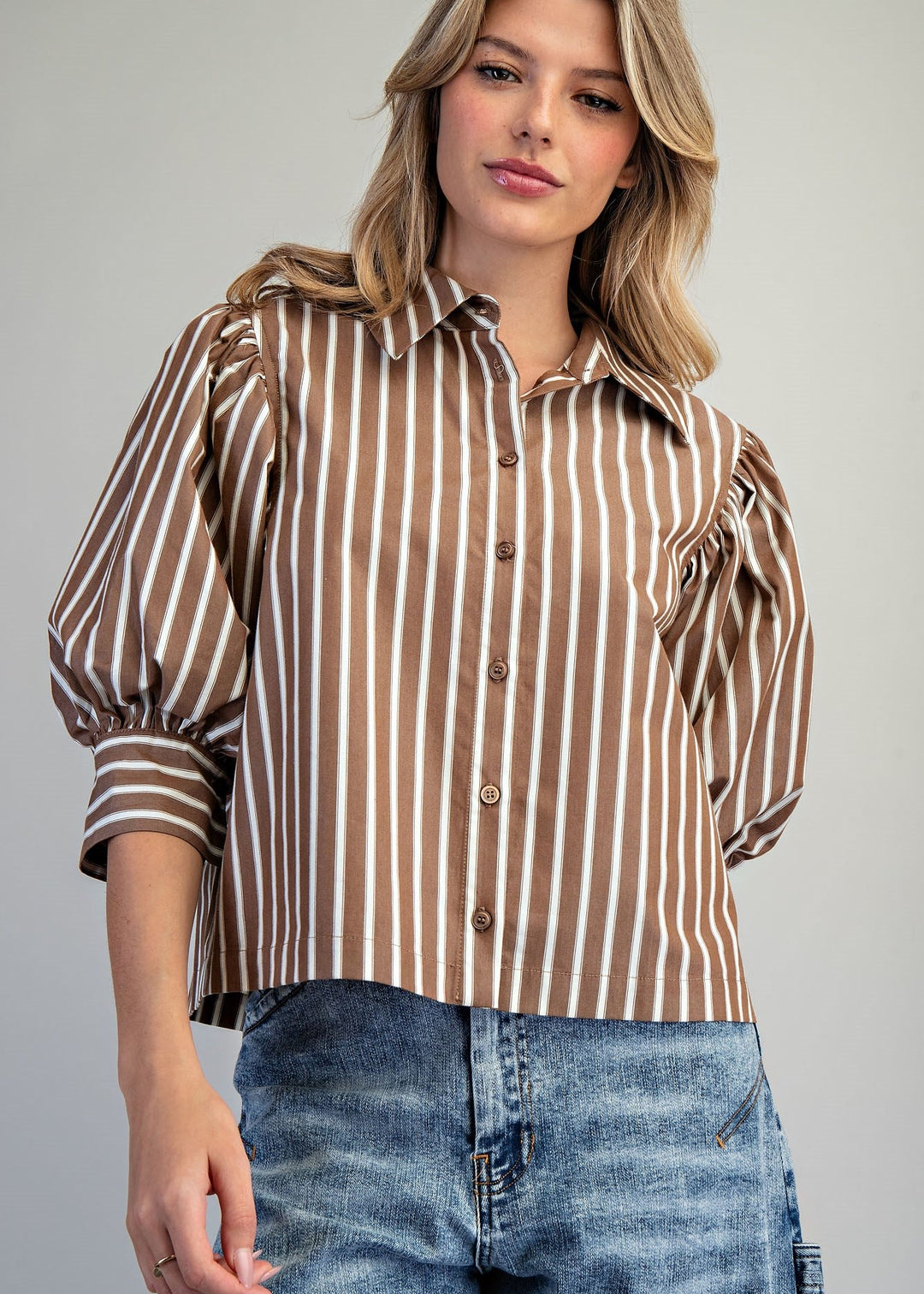 Woman wearing brown and white stripe puff sleeve blouse and denim jeans on white background
