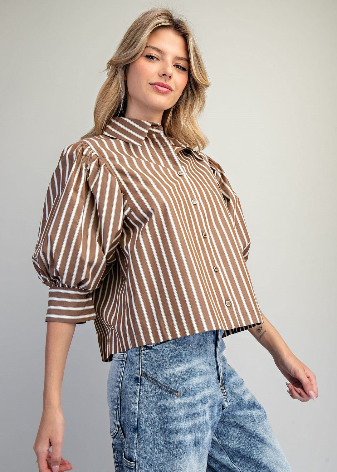 Woman wearing brown and white stripe puff sleeve blouse and denim jeans on white background