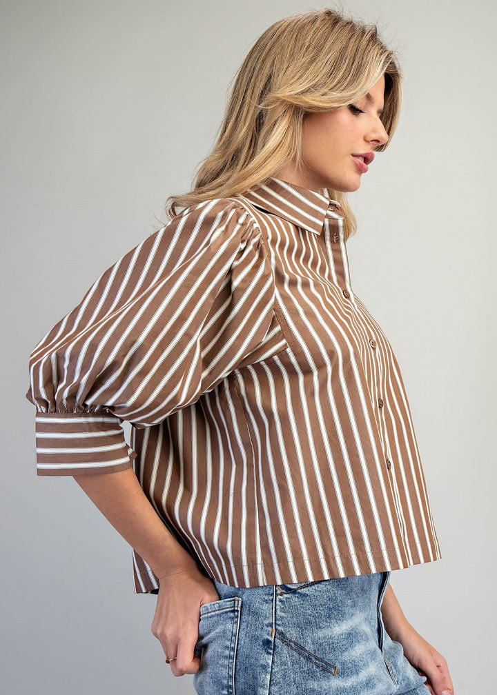 Woman wearing a brown and white striped shirt with blue jeans on a plain background