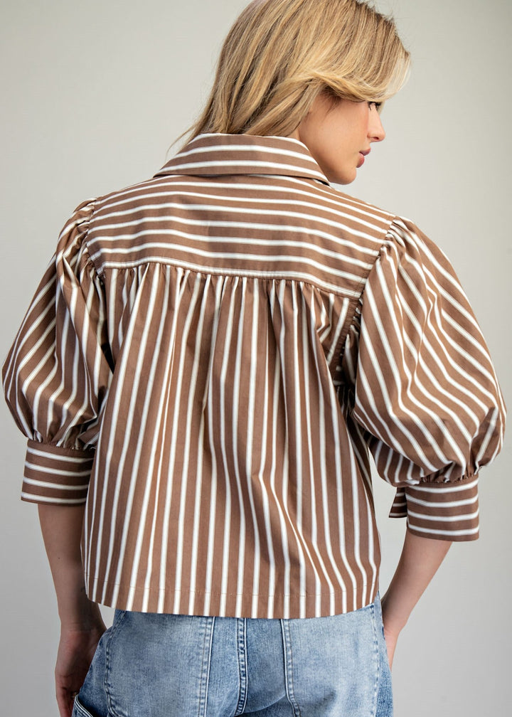 Person wearing a brown and white striped shirt with rolled-up sleeves and blue jeans on a plain background