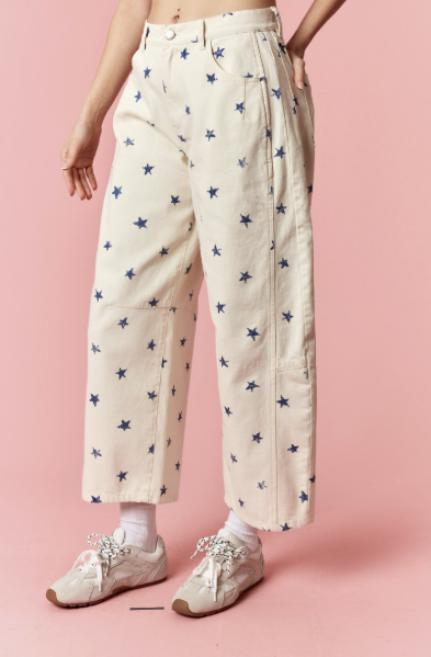 Person wearing cream pants with blue star pattern and white sneakers on a pink background