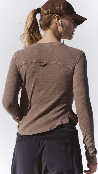 Woman shown from back wearing brown long sleeve top, baseball cap and black pants on white background