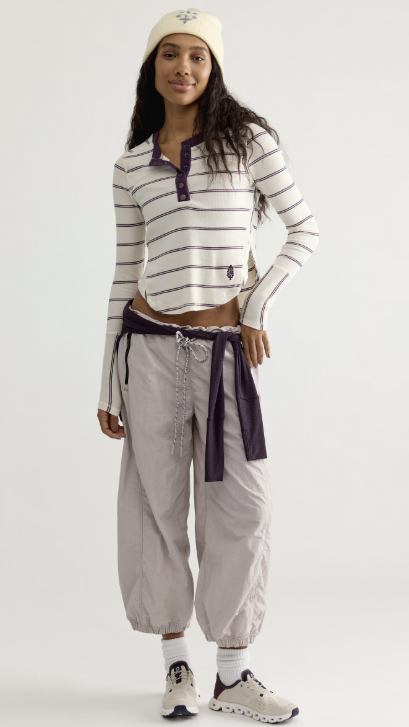 Woman wearing white and purple stripe top with beige pants on white background