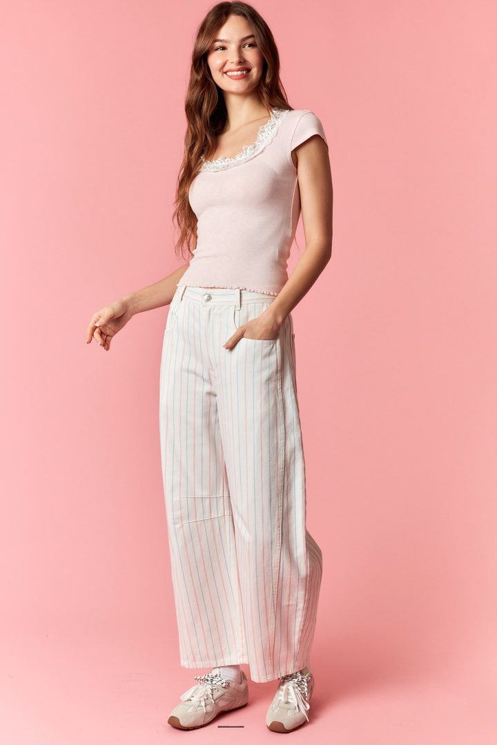 Woman wearing a white top and striped pants on a pink background