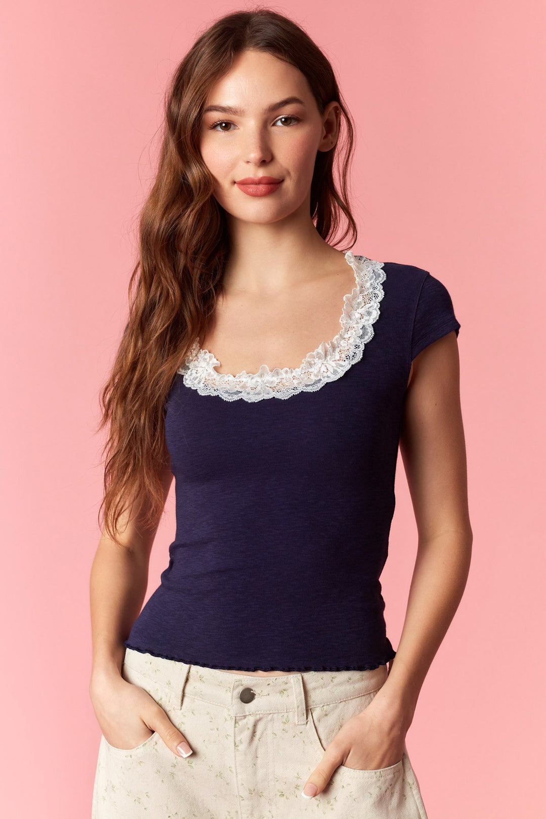 Woman wearing a navy blue top with lace neckline against a pink background