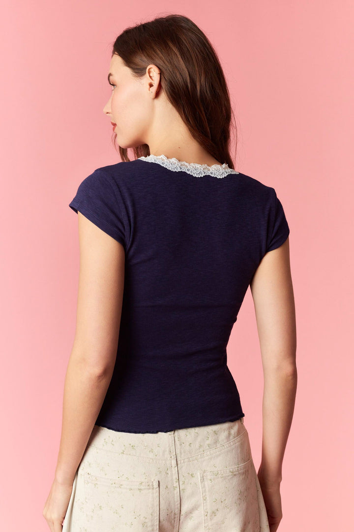 Woman wearing a navy blue top with lace neckline on a pink background