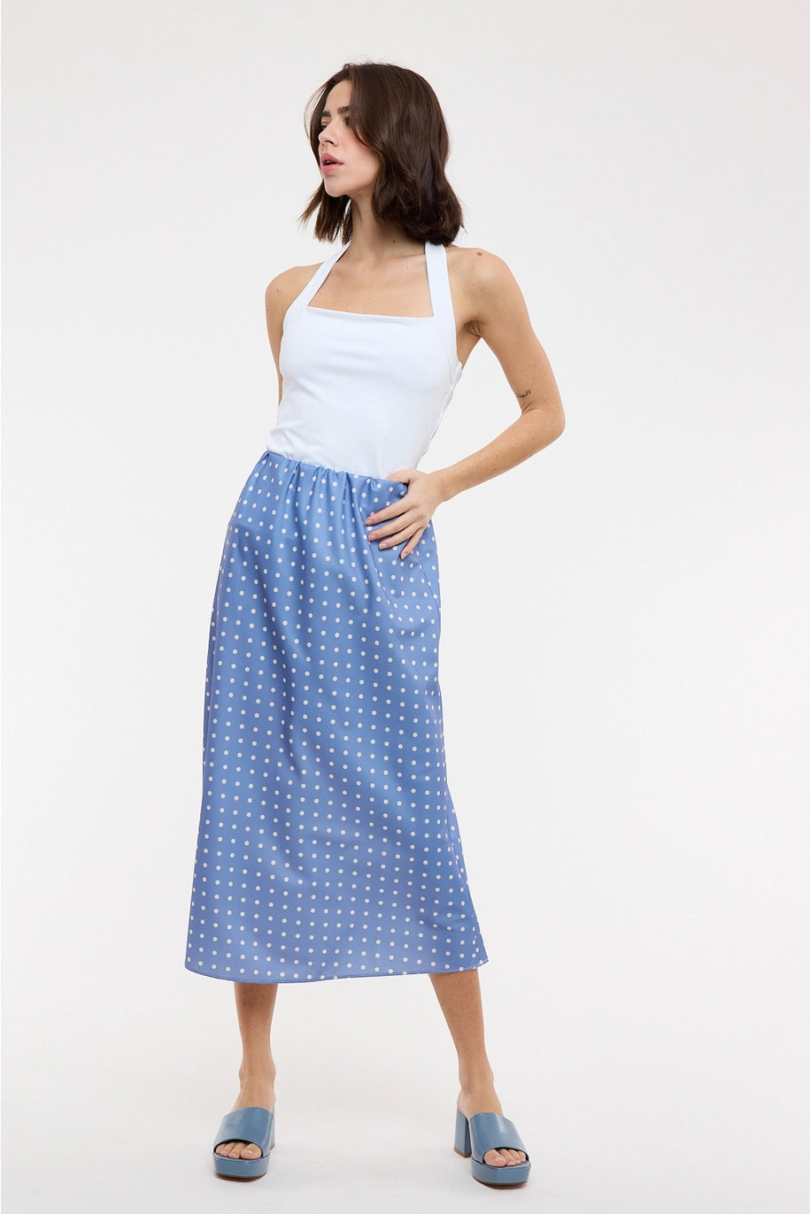 Woman wearing blue polka dot midi satin skirt and white halter top on plain background