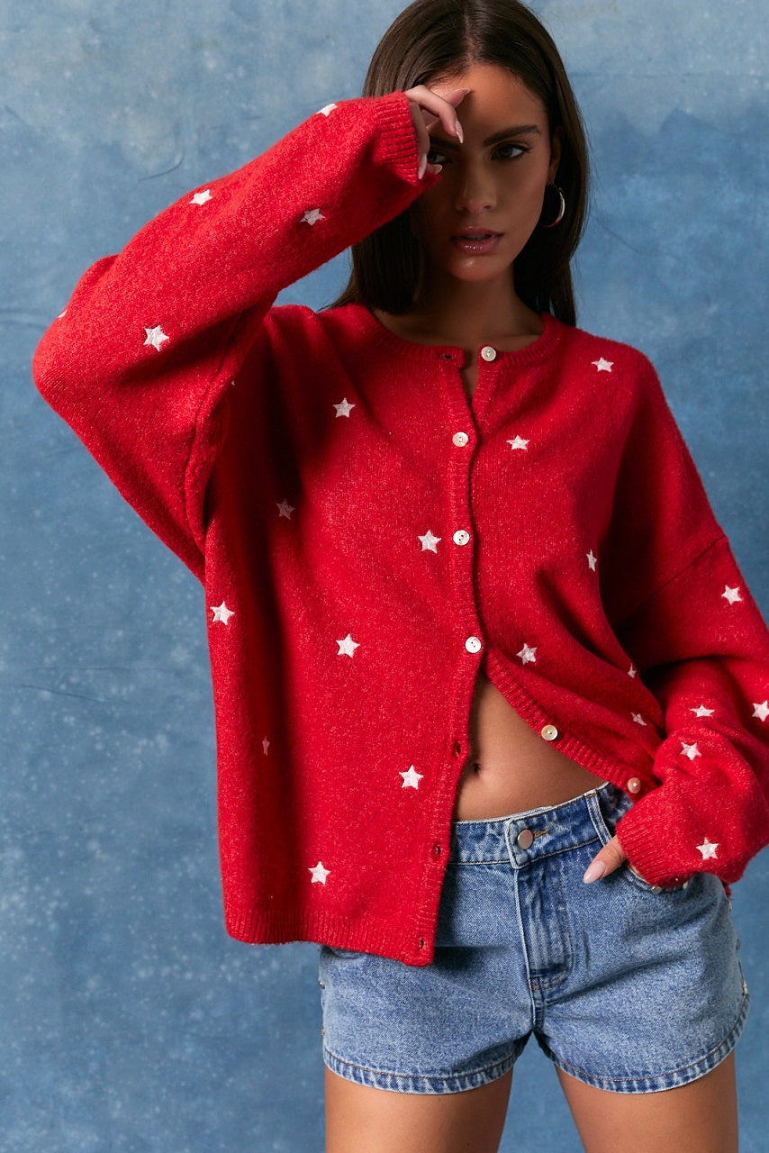 Woman wearing red cardigan with white stars and blue jeans shorts on blue background