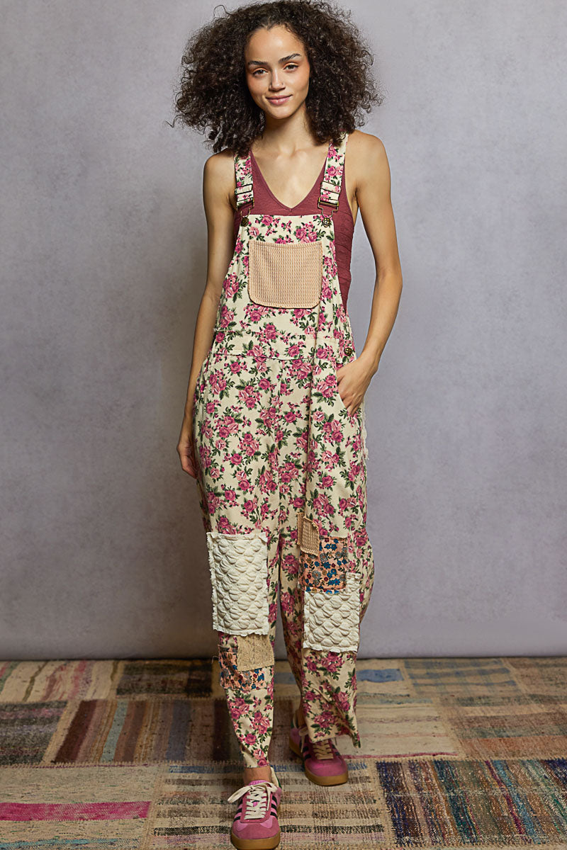 Woman wearing a floral overalls with a plain top against a gray wall.