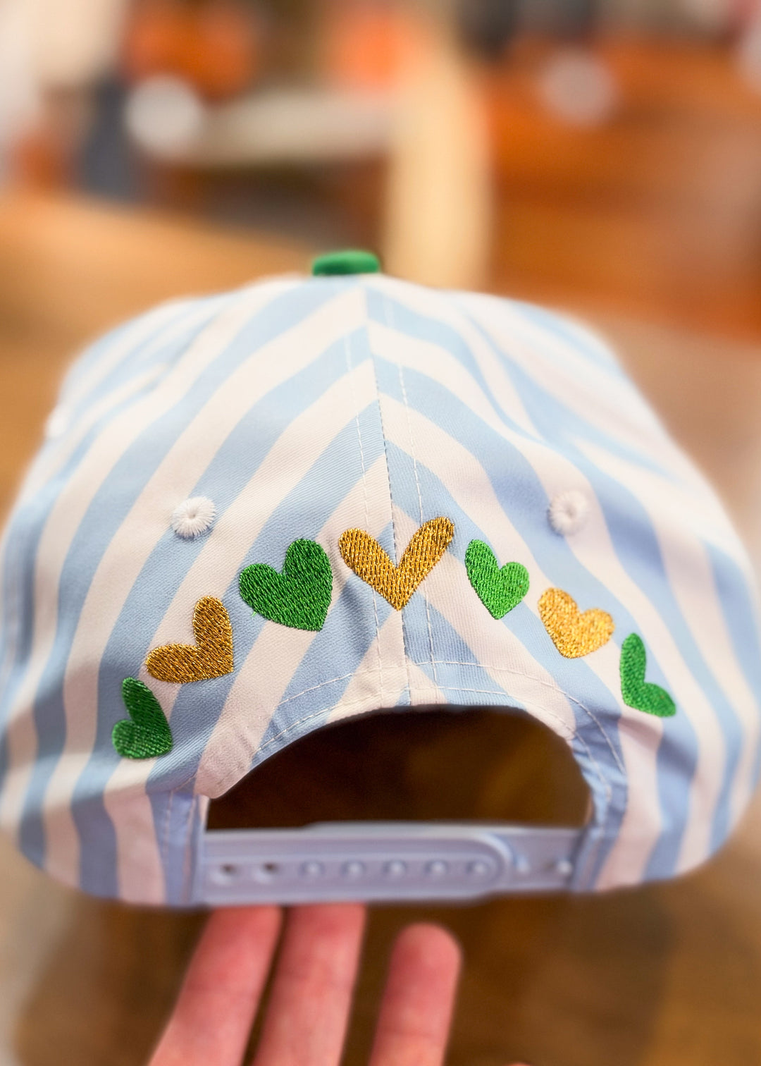 blue and white stripe trucker hat with gold and green hearts embroidered across back