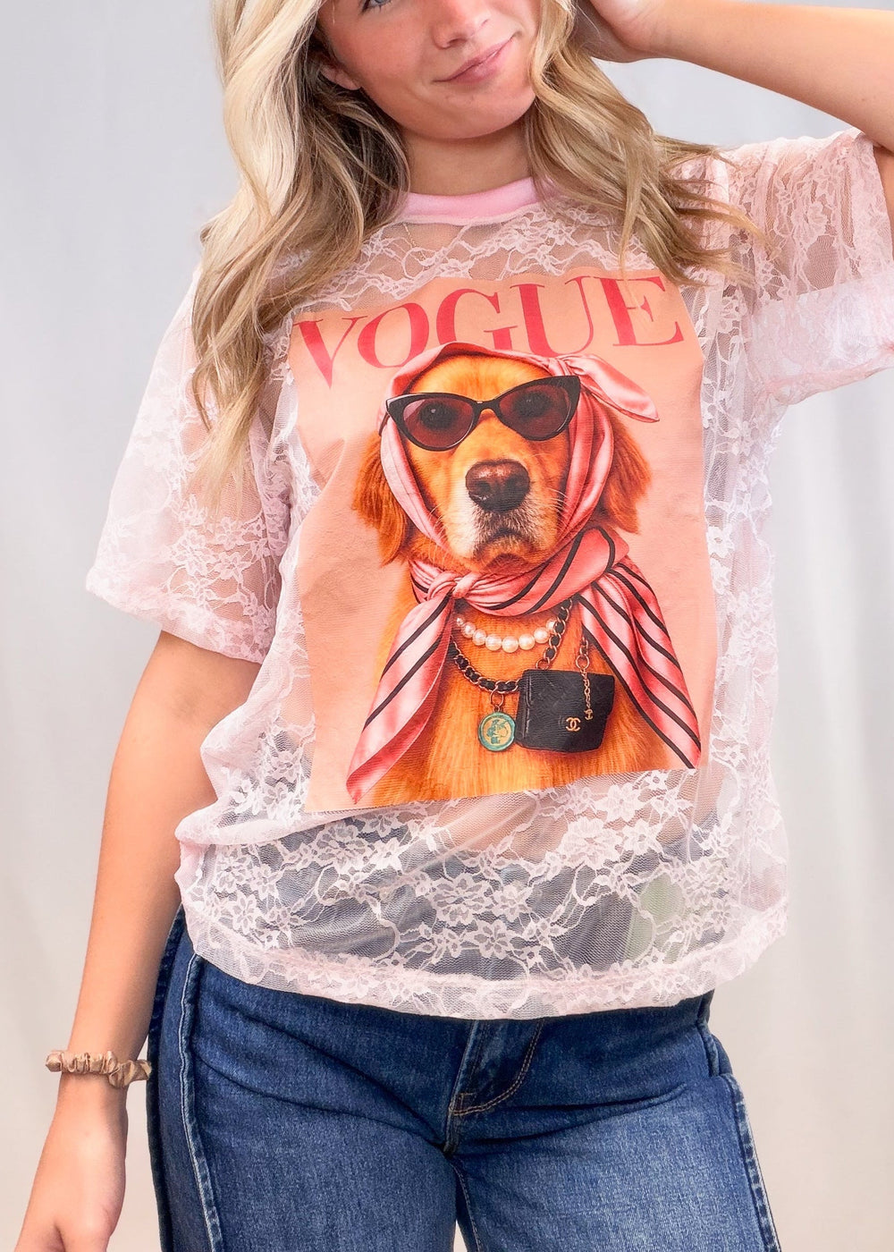 Woman wearing pink lace tee with golden retriever graphic on front with denim jeans on plain background