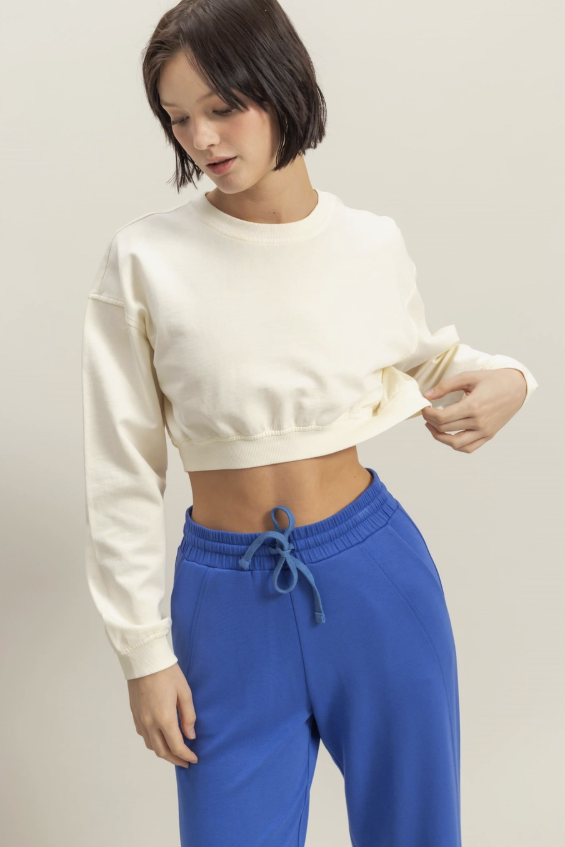 Woman wearing cream pullover and blue sweatpants on plain background