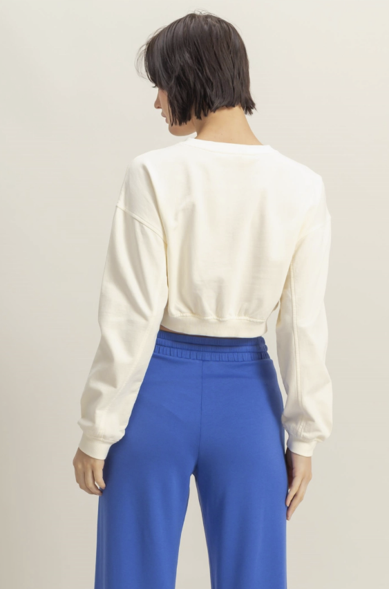 Person wearing a white sweater and blue pants against a plain background